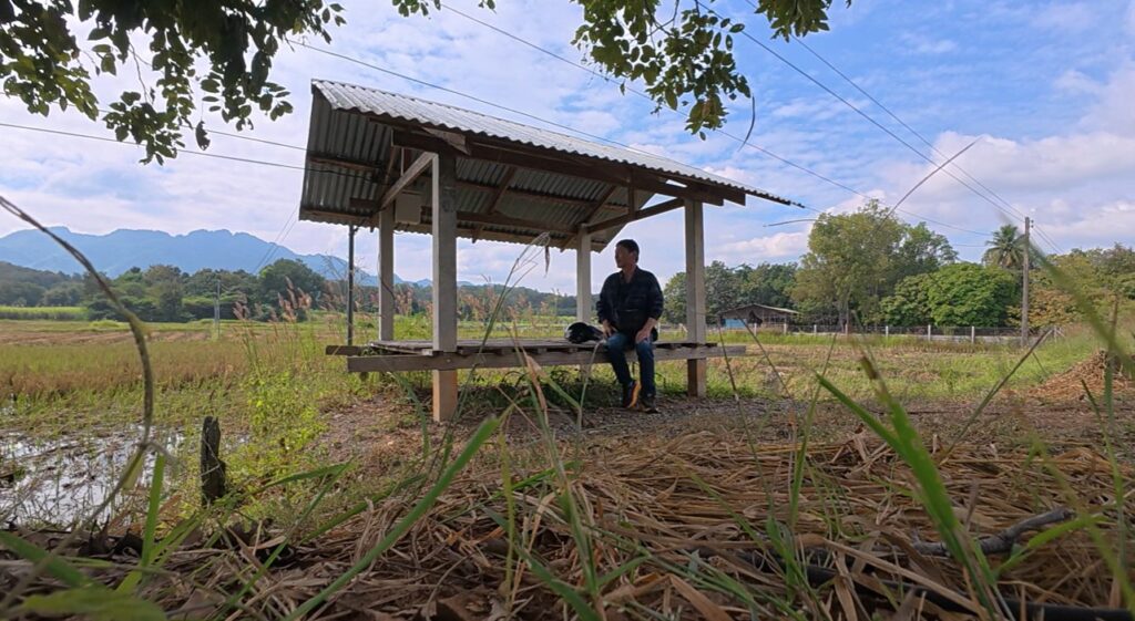 Rider resting at a peaceful roadside shelter in rural Thailand