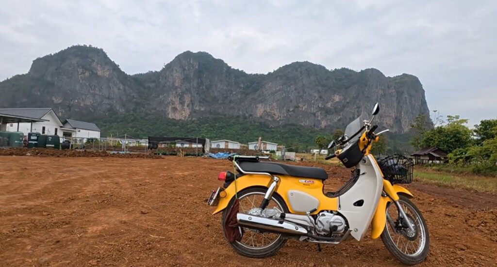 Yellow Honda Super Cub beneath the limestone mountains of Pha Man, Thailand