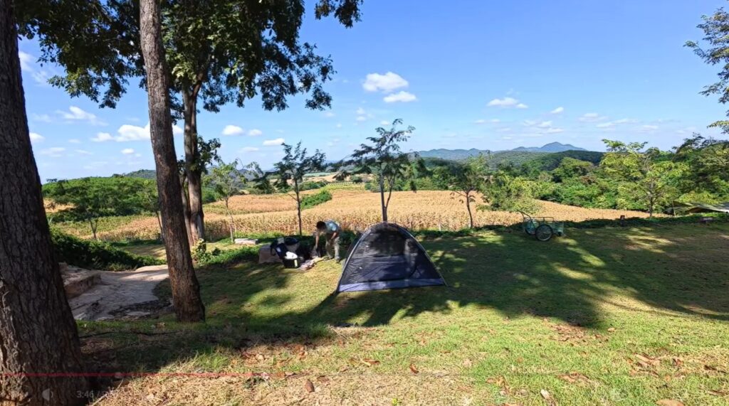 Setting up a tent beneath shady trees at a peaceful campsite in rural Thailand