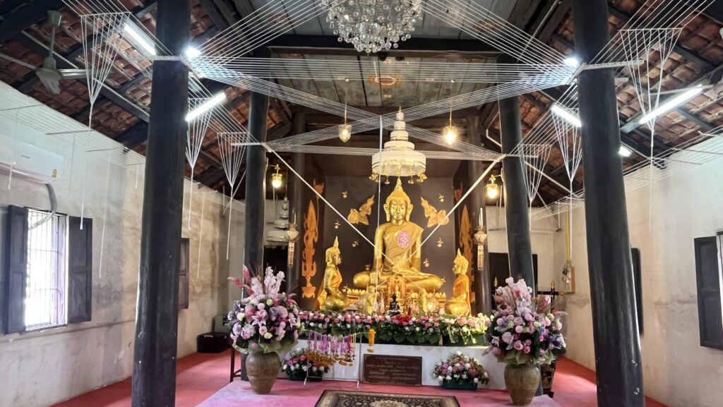 Golden Buddha beneath sacred Sai Sin threads inside the ancient ubosot