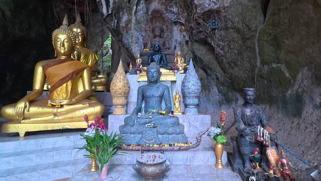 Small statue of King Naresuan among sacred images inside a cave temple in Rayong