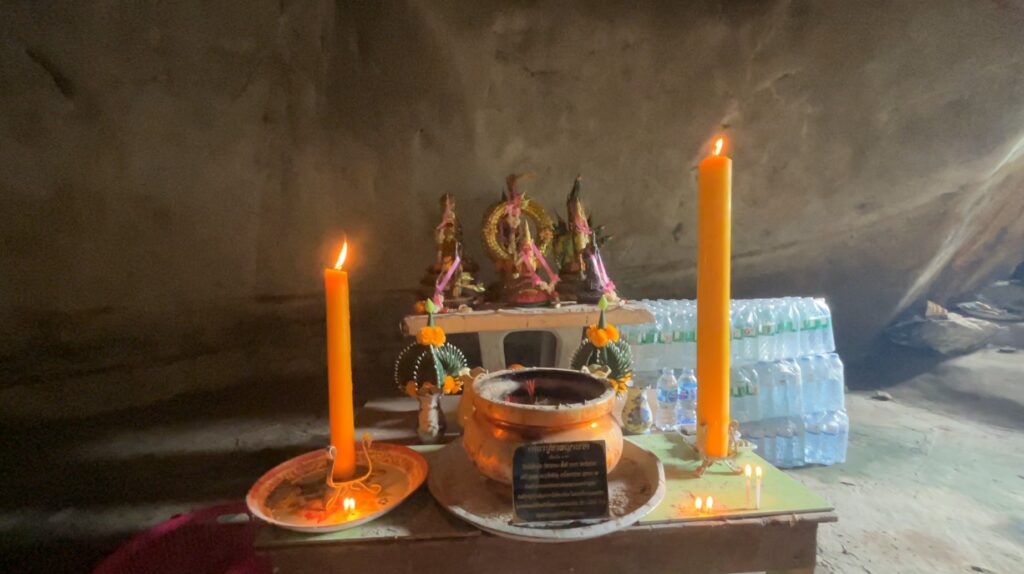 Candlelit Hindu sacred figures inside a dark chamber of Tham Khao Bot cave