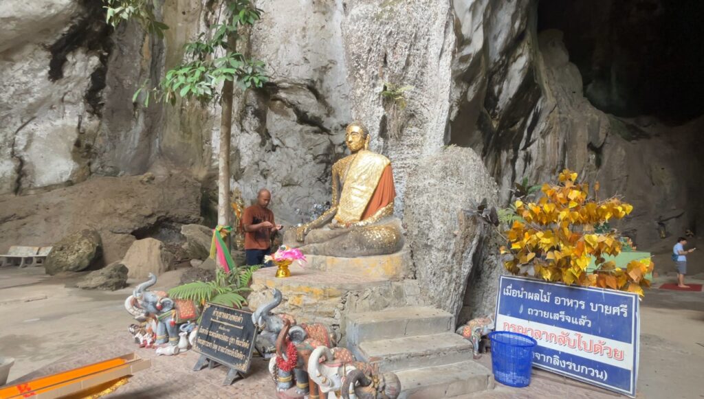 Old seated Buddha beneath the natural limestone wall inside Tham Khao Bot cave