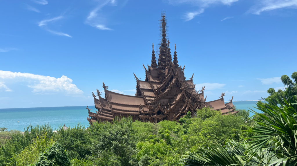 The Sanctuary of Truth appearing through tropical trees beside the blue sea in Pattaya